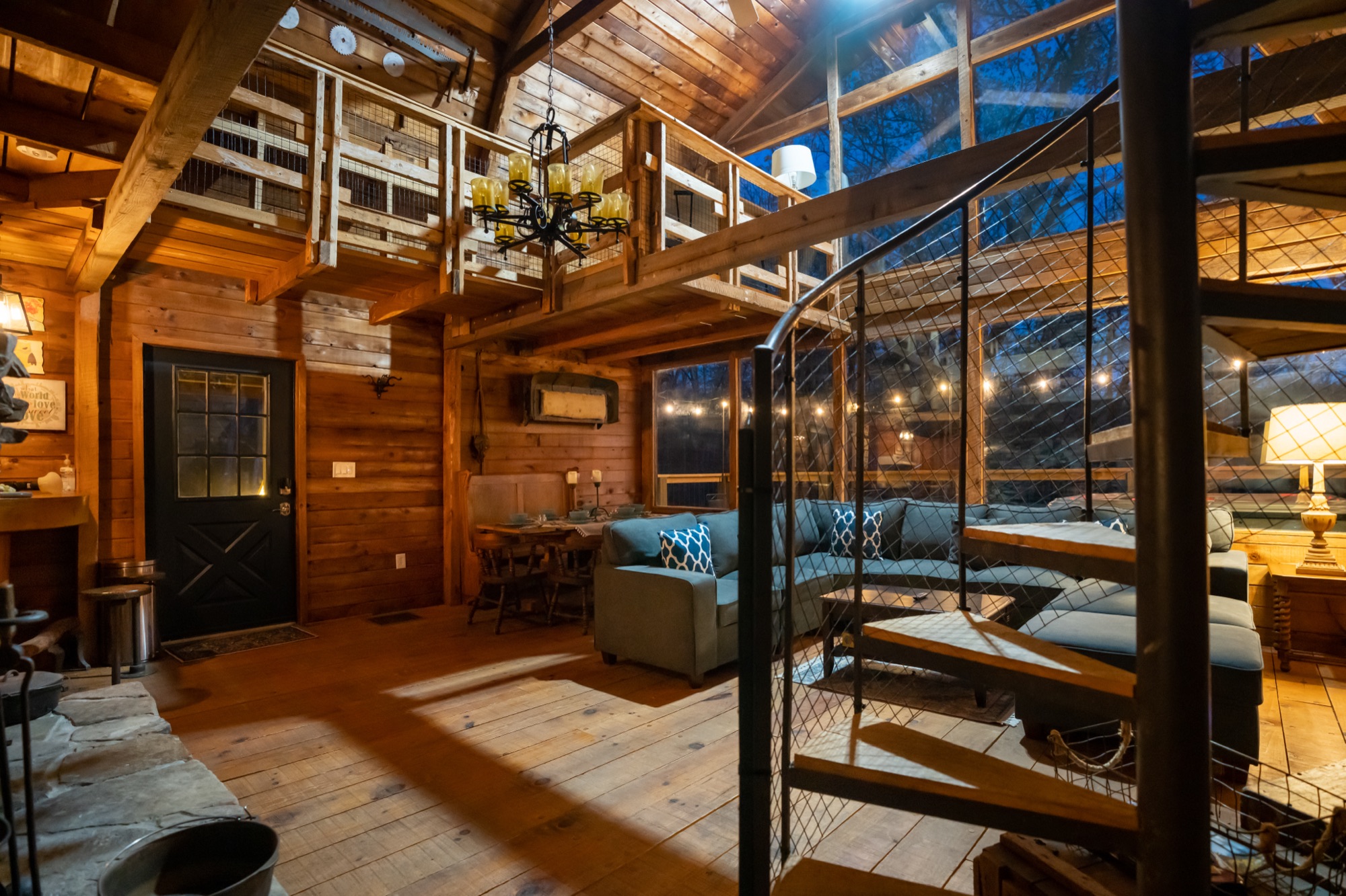 Rustic Retreat living room at night with a blue-gray sectional and view up the spiral staircase to the loft